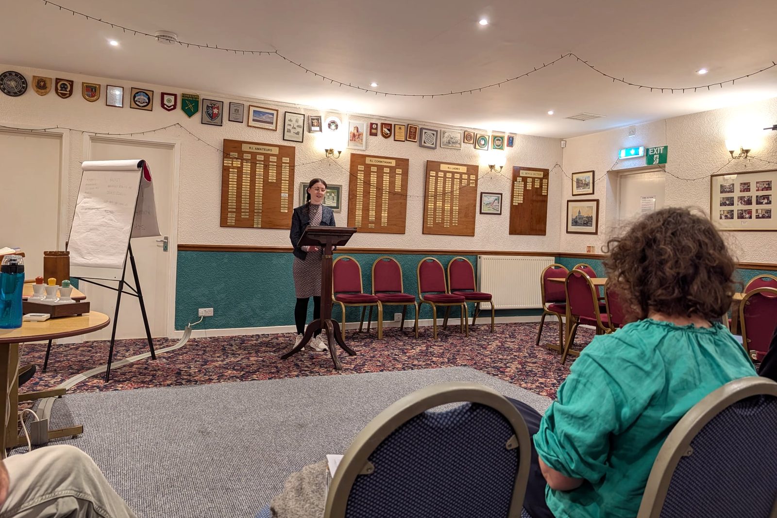 A member speaking at the lectern during a club night, with the audience seated in front